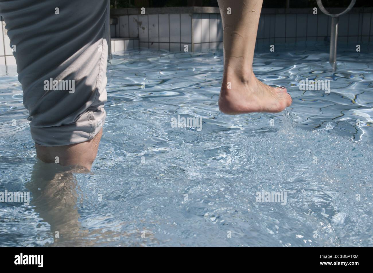 Foto esterna di gambe femminili che camminano in acqua (cura Kneipp) in una piscina piastrellata con corrimano in acciaio inox Foto Stock
