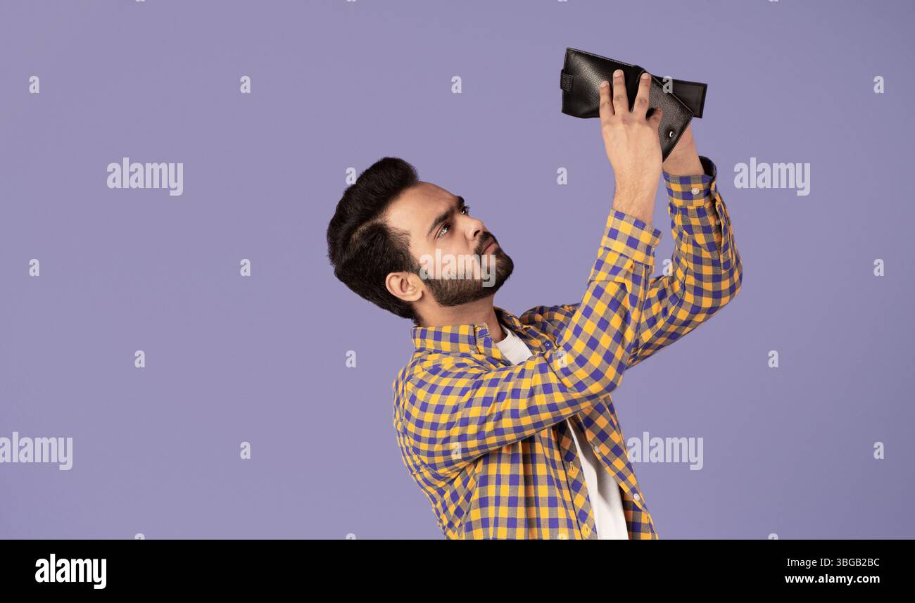 Concetto di crisi economica. Un ragazzo indiano sconvolto con un portafoglio vuoto su sfondo viola Foto Stock