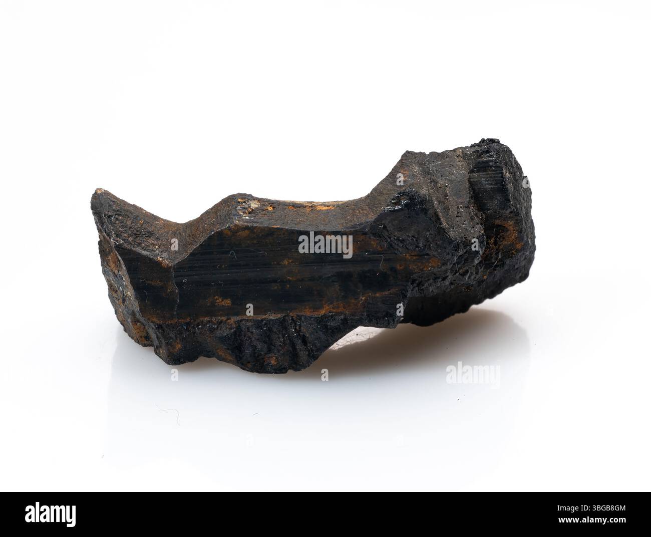 Un frammento di cristallo di tormalina nera grezzo e non tagliato si erge in modo prominente su uno sfondo bianco pulito, mostrando la sua consistenza naturale, striata e profonda, Foto Stock