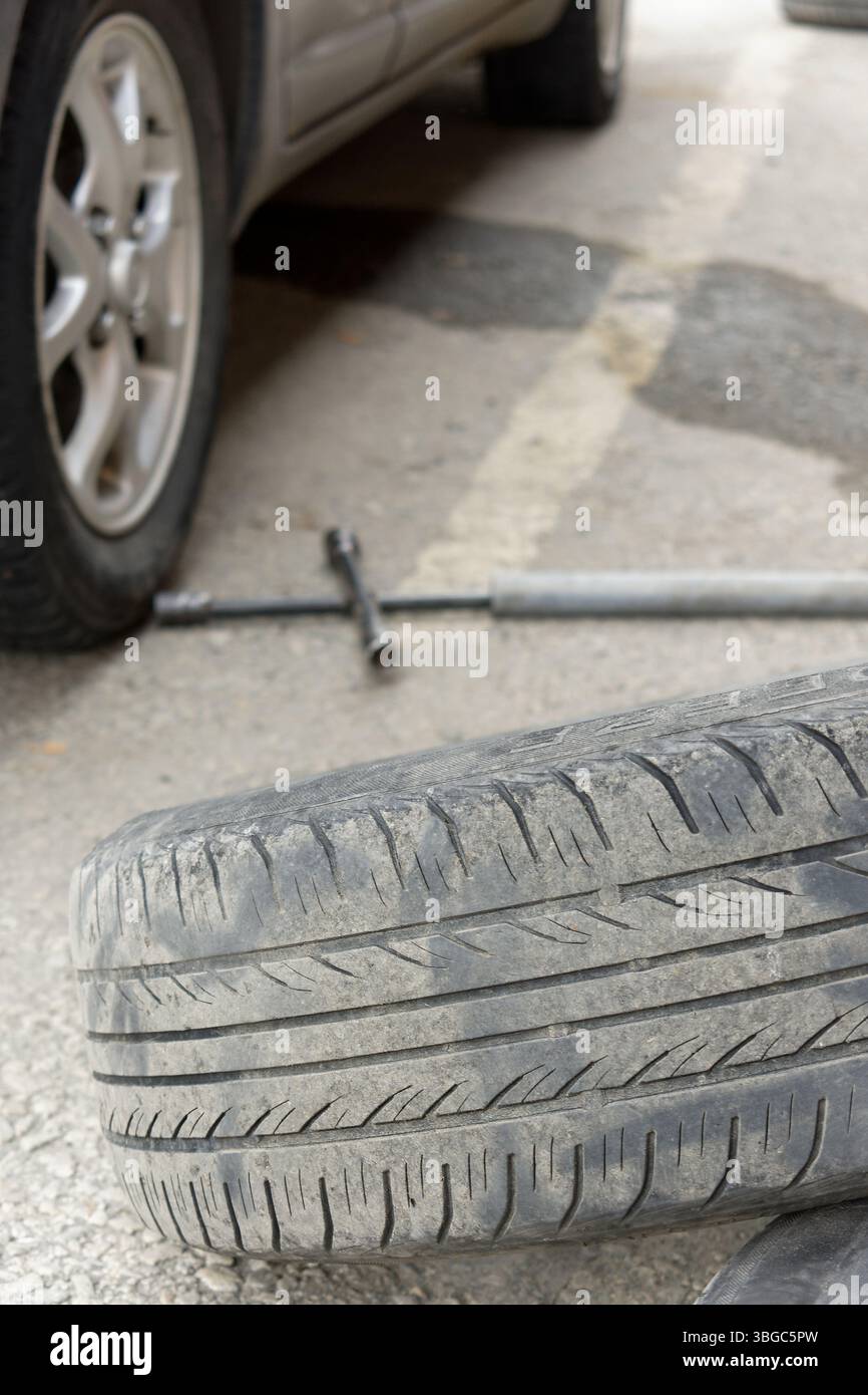 L'immagine cattura una scena stradale della sostituzione di uno pneumatico di un'auto. Uno pneumatico sgonfio è a terra e una chiave a bussola è nelle vicinanze, evidenziando la necessità di aut Foto Stock
