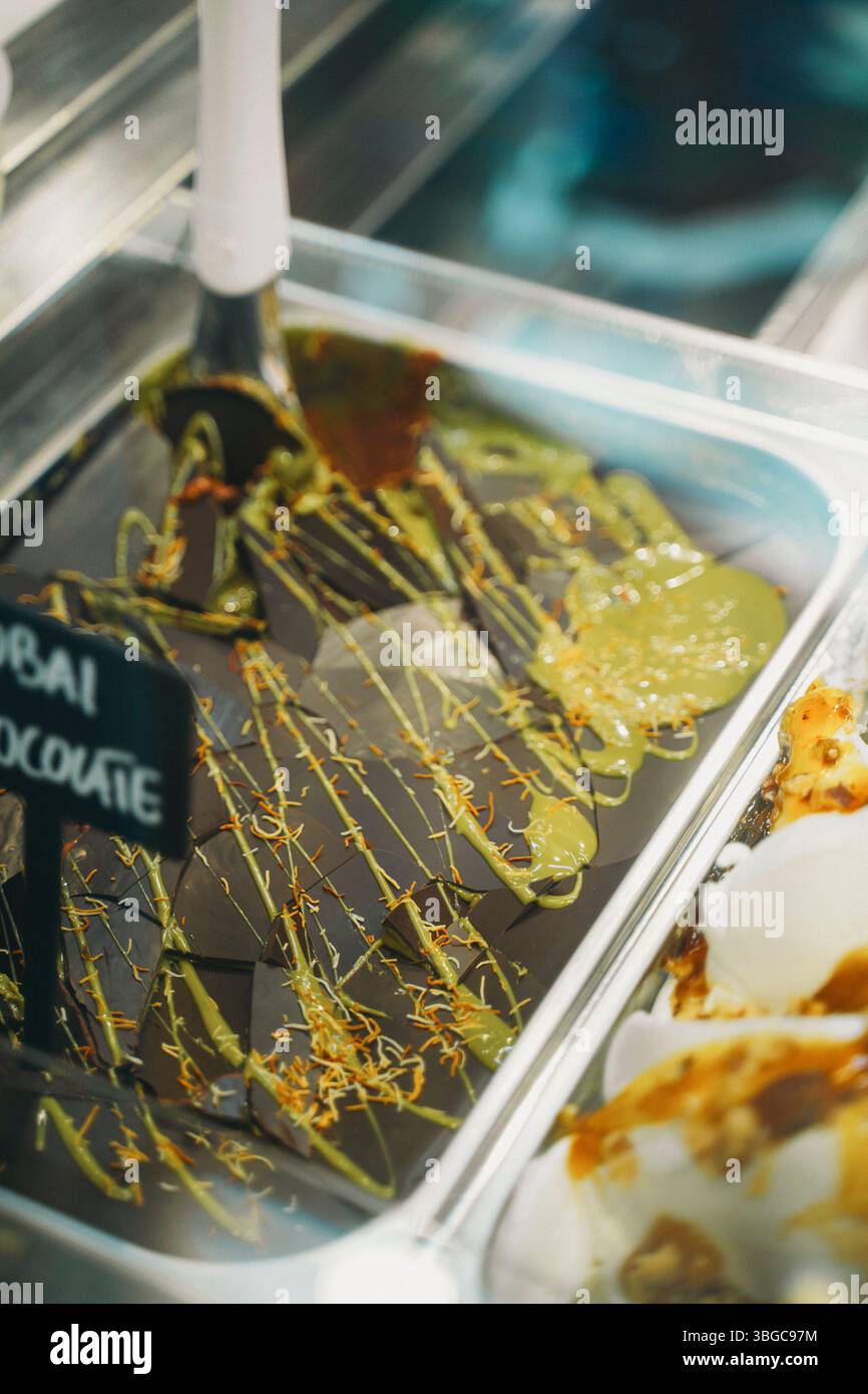 Gelato al cioccolato e Matcha con condimenti decorativi esposti in un contenitore di metallo presso un negozio di dolci. La texture ricca e i colori vivaci creano una e. Foto Stock