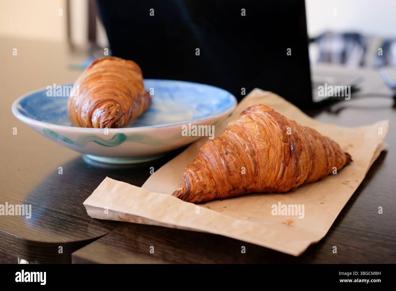 Pausa lavoro Bliss. Croissant e una pausa per laptop. Spuntino sulla scrivania accanto al portatile. Lavoro in remoto. Foto Stock
