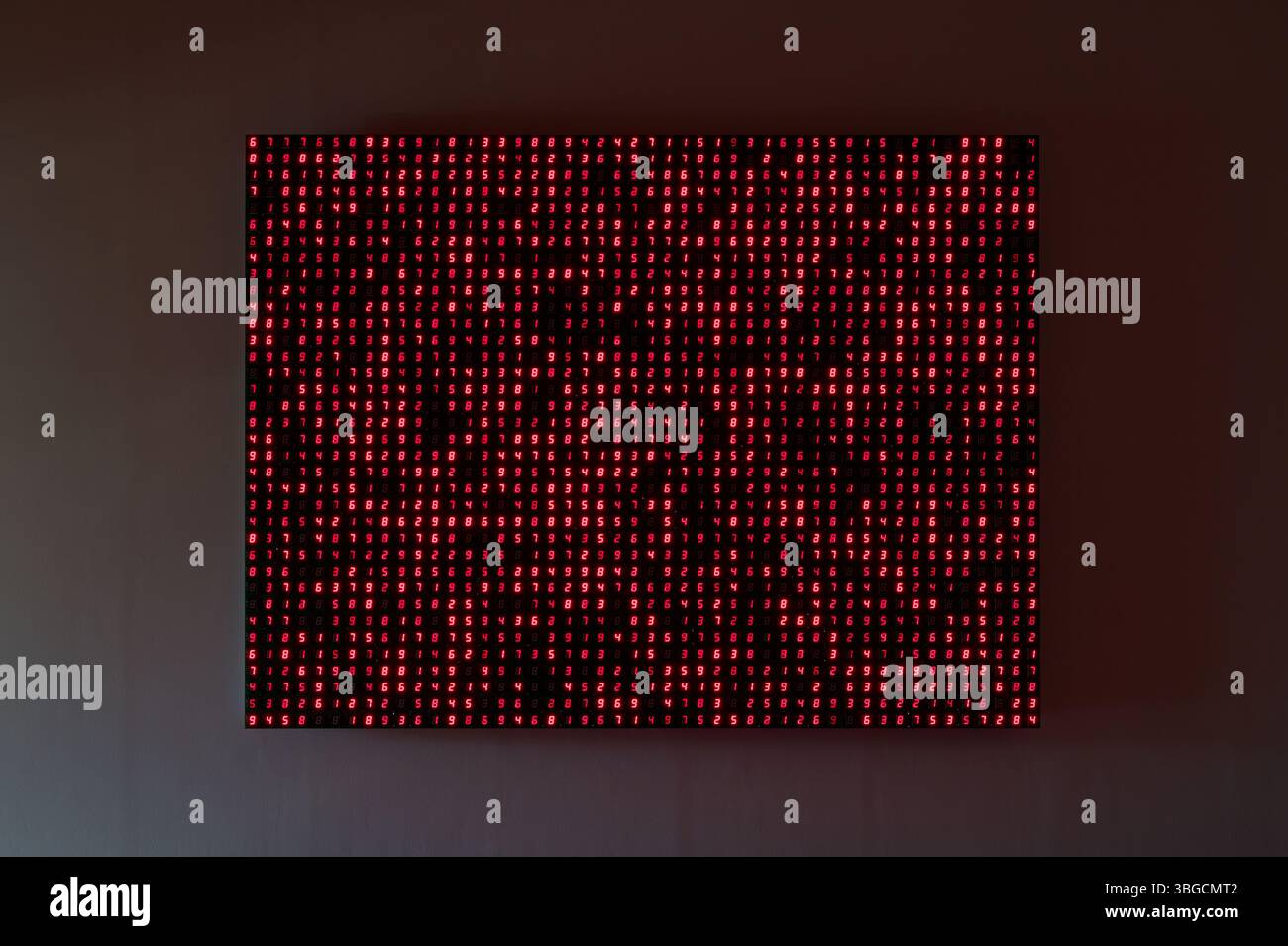 La brillante matrice di dati dei numeri rossi in continuo mutamento illumina una parete scura Foto Stock