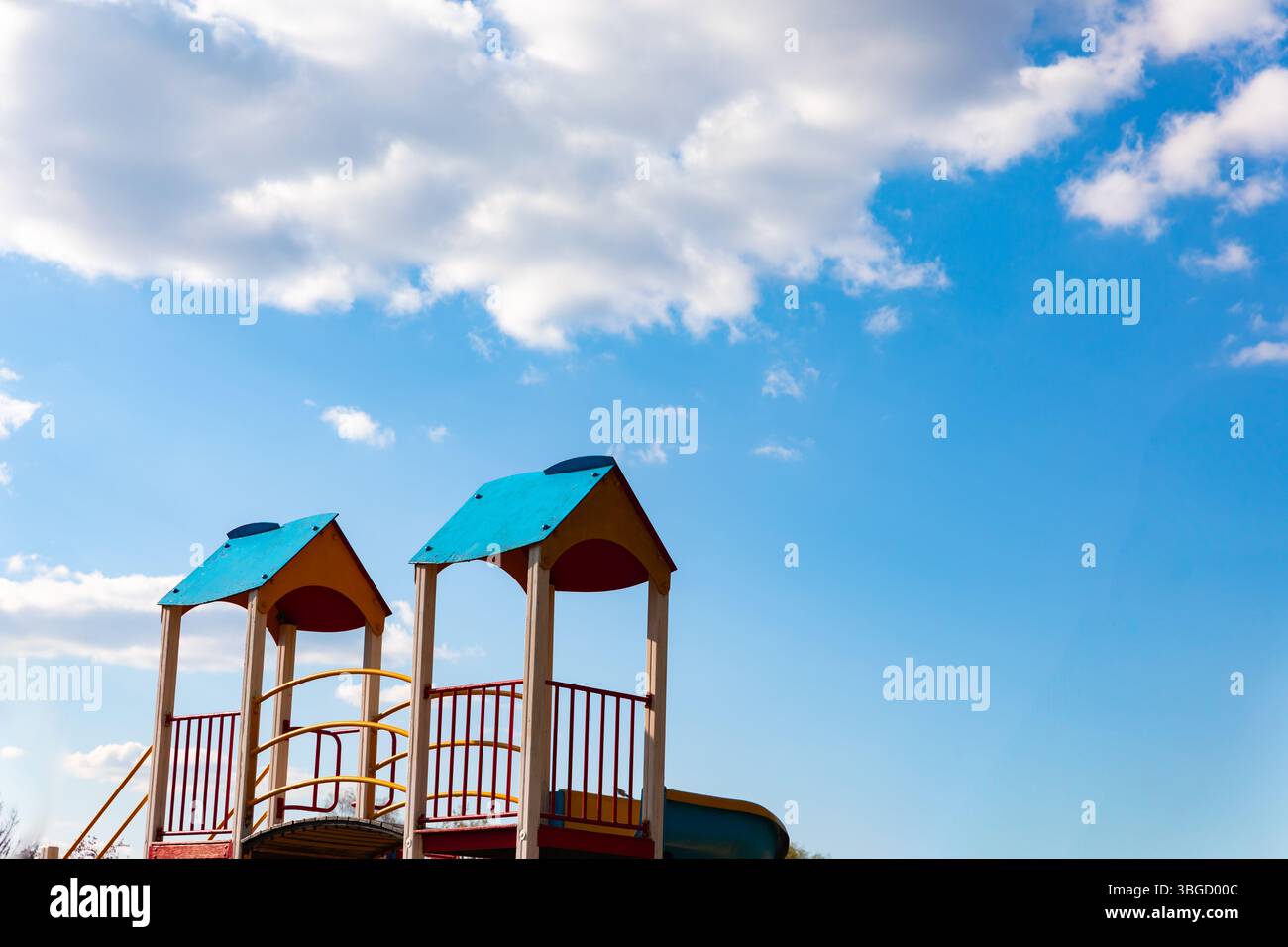 Colorate torri di parco giochi con tetti blu adagiati su un cielo luminoso con morbide nuvole, che evocano un'atmosfera allegra e giocosa. Foto Stock