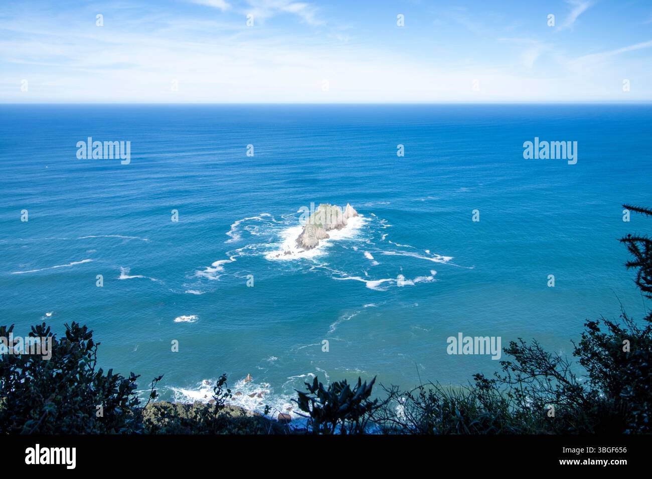 Vista mozzafiato di un piccolo isolotto roccioso circondato dalla vastità dell'oceano blu profondo, con un cielo sereno e nuvoloso in alto Foto Stock