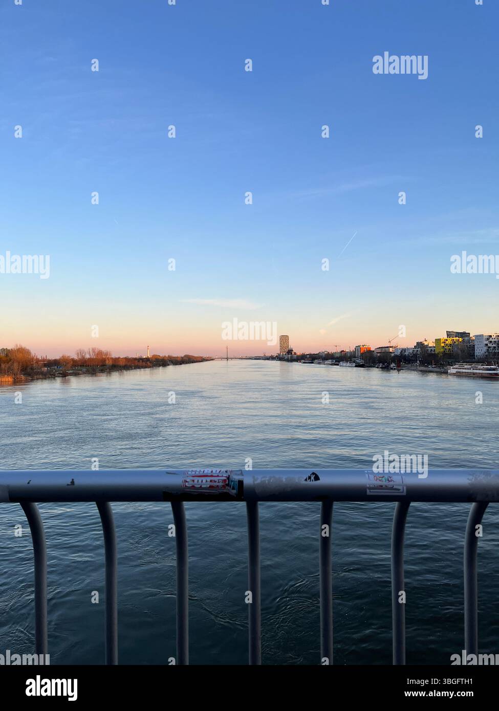 Vista da un ponte che si affaccia su un fiume calmo al tramonto con il paesaggio urbano e moderno grattacielo in lontananza. Foto Stock