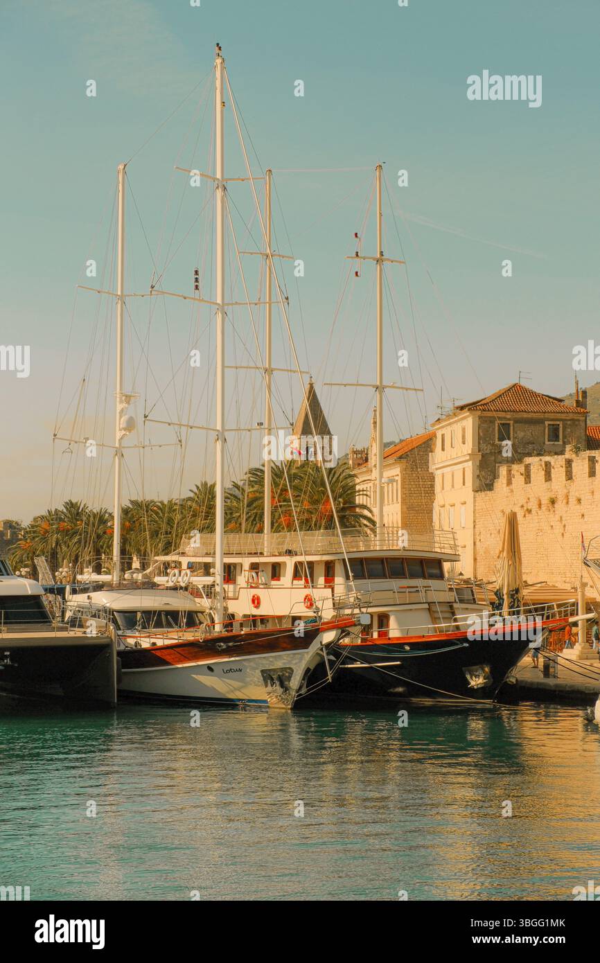 Porto di Traù, Croazia, con barche a vela e yacht attraccati sul lungomare vicino a edifici storici in pietra e palme. Foto Stock