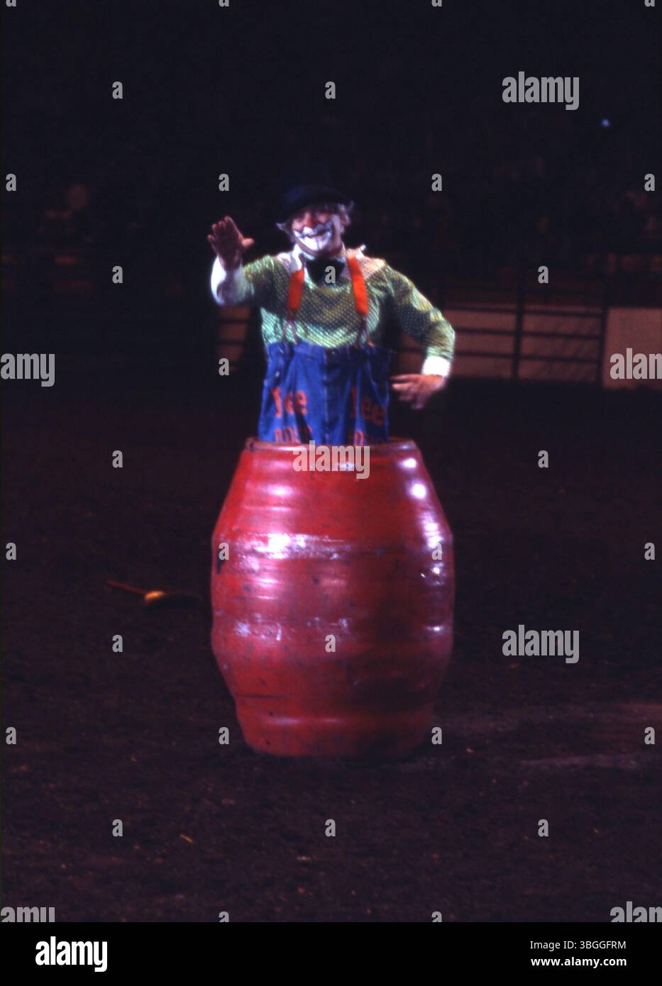 Un clown rodeo non identificato si erge in una canna rossa con pantaloni blu con bretelle arancioni. I suoi pantaloni sono stampati con 'Jee Rodeos'. L'immagine cattura un tipico momento di clown del rodeo, mettendo in evidenza il suo vestito e il ruolo comico durante un evento di rodeo. Foto Stock