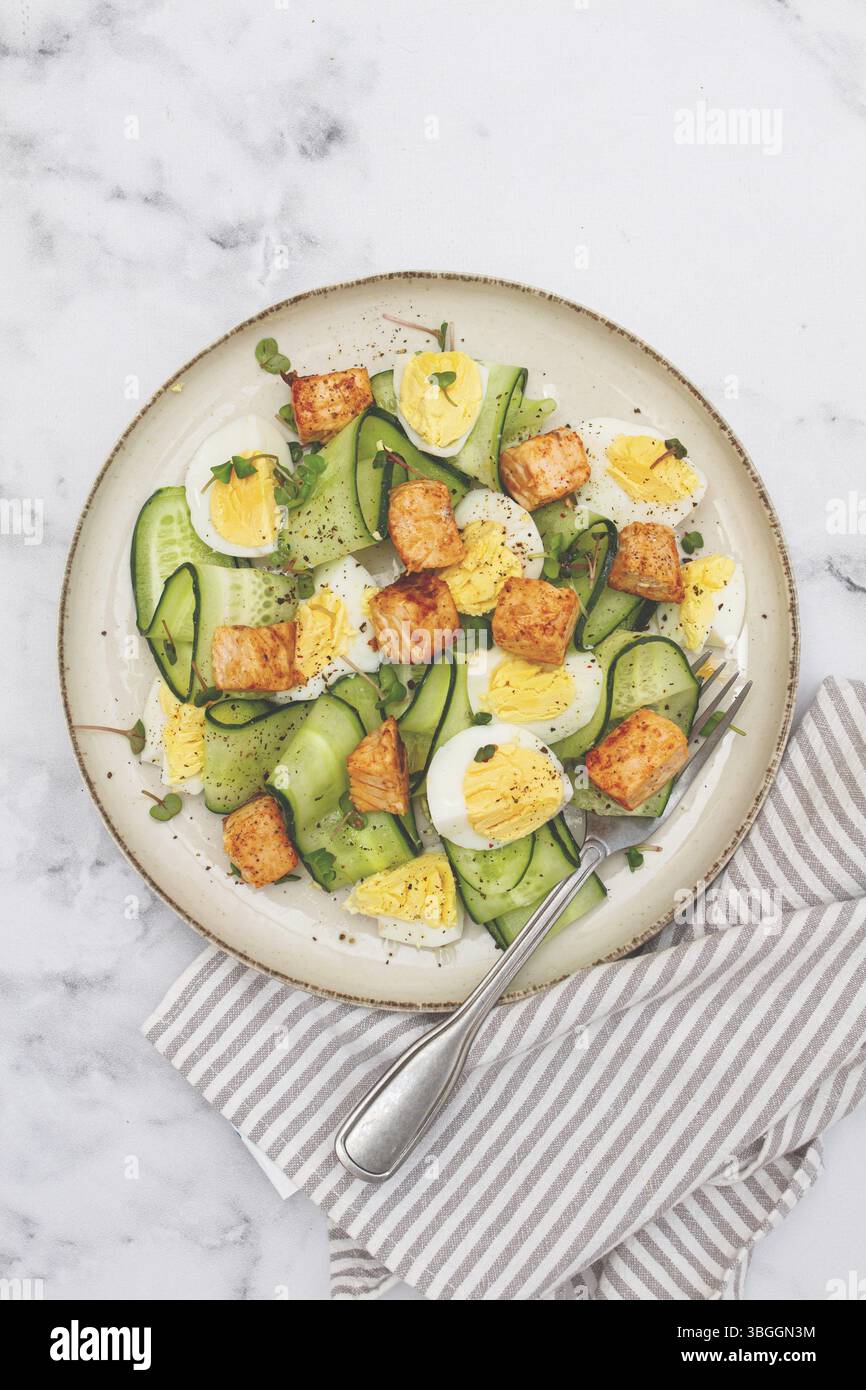 Deliziosa insalata di salmone e uova servita su un piatto con cetriolo fresco ed erbe aromatiche per un pasto sano all'ora di pranzo Foto Stock