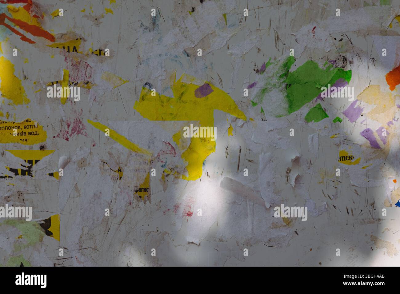 Una bacheca resistente agli agenti atmosferici con frammenti di carta colorati e poster strappati, creando uno sfondo strutturato e astratto. Strati di carta grunge frammentati Foto Stock