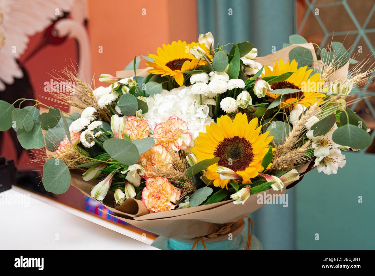 Bellissimo bouquet legato a mano con girasoli, gambi di grano, garofani e vegetazione, perfetto per matrimoni rustici o regali di stagione. Foto Stock