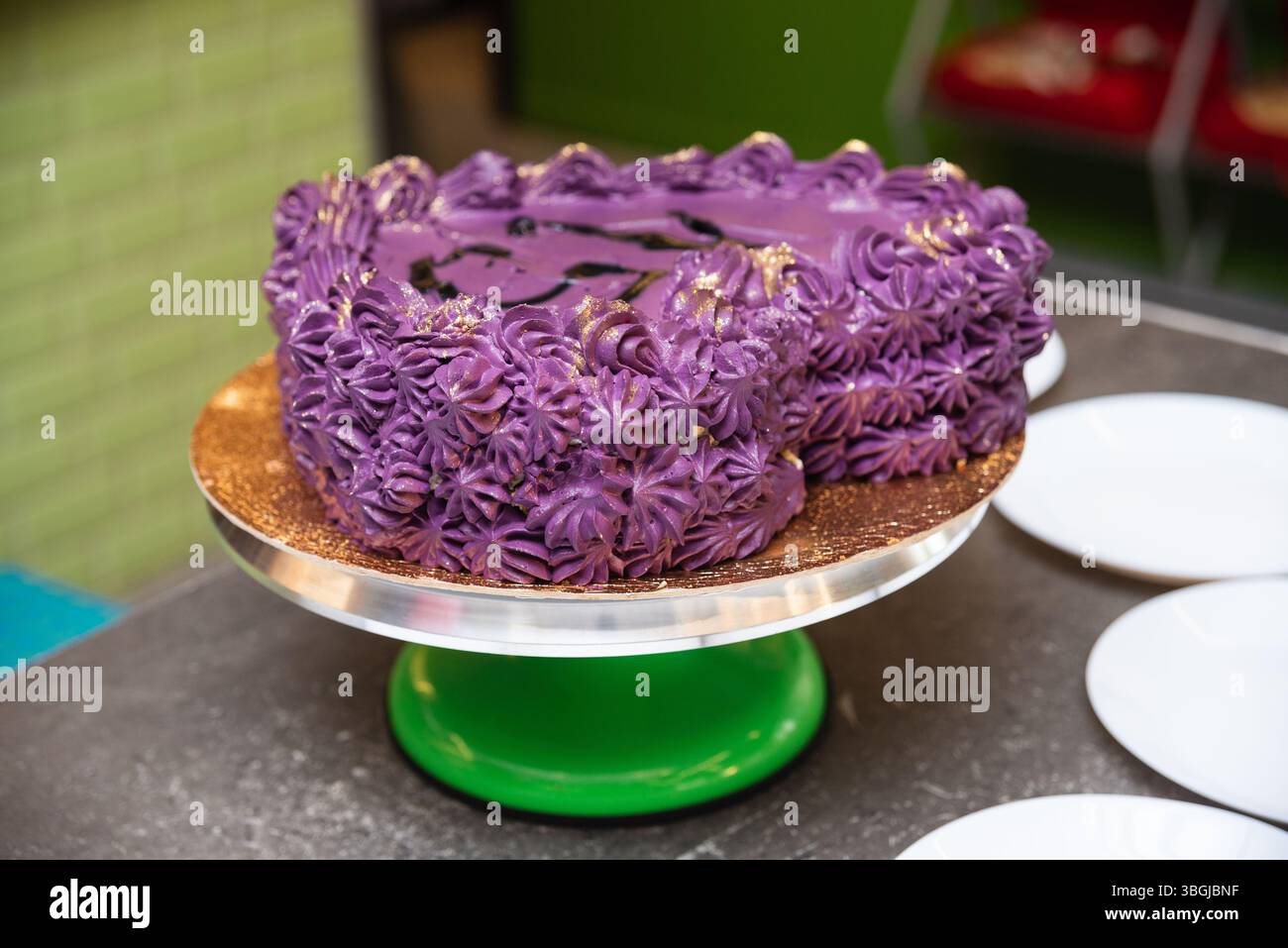 Torta decorativa con glassa viola e polvere d'oro, esposta su un supporto per torta verde, ideale per feste o feste. Foto Stock