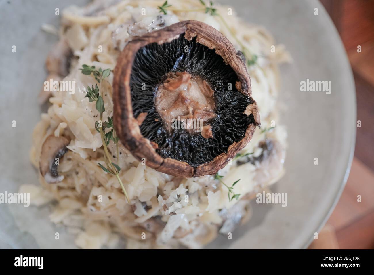 Delizioso risotto ai funghi condito con un grande fungo portobello, guarnito con erbe fresche, che presenta un piatto italiano ricco e cremoso. Foto Stock