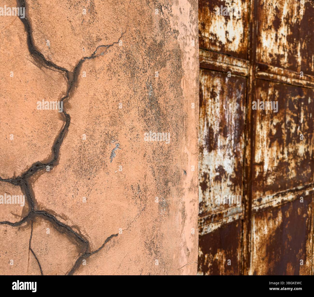 Parete intonacata incrinata con fratture profonde e superficie ruvida, cancello in metallo arrugginito parzialmente visibile. Adatto per texture, decadimento, sfondi, design. Foto Stock