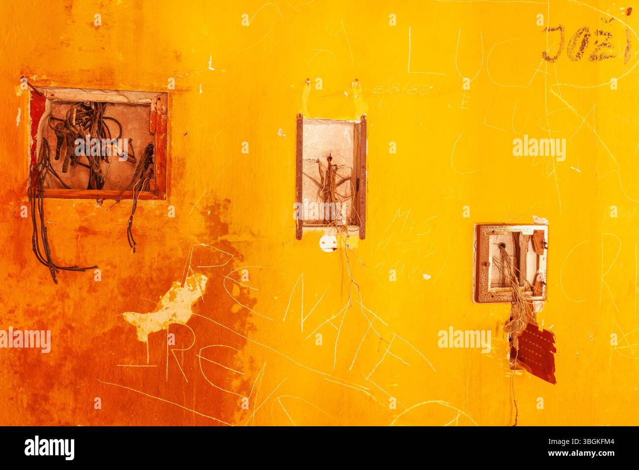 Parete arancione intemprata di un edificio abbandonato con graffiti e cavi elettrici sospesi, che mostrano segni di degrado urbano Foto Stock