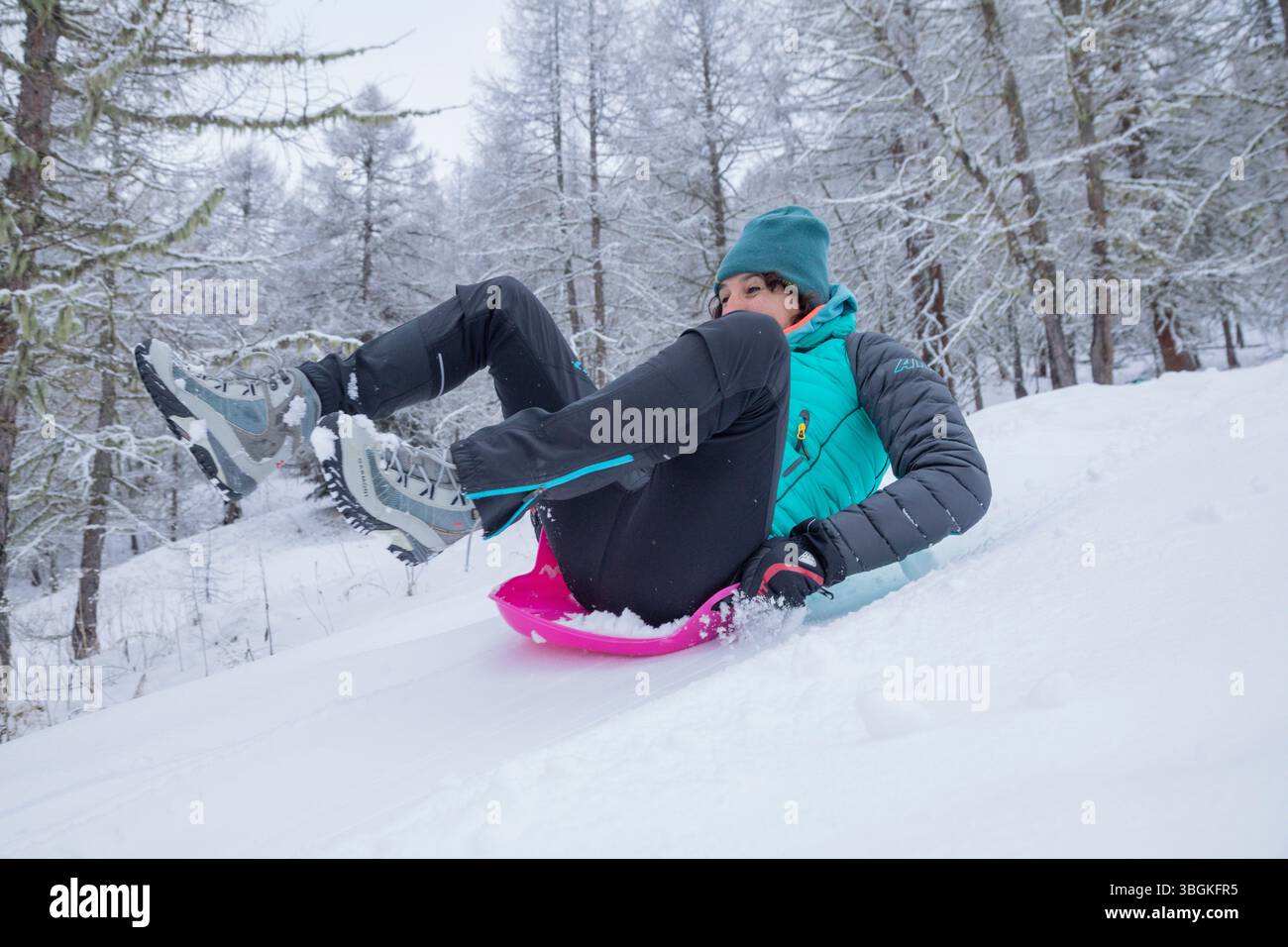 Donna, 45 anni, che si gode una divertente giornata invernale, che fa slittino sulla neve fresca con abbigliamento sportivo colorato Foto Stock