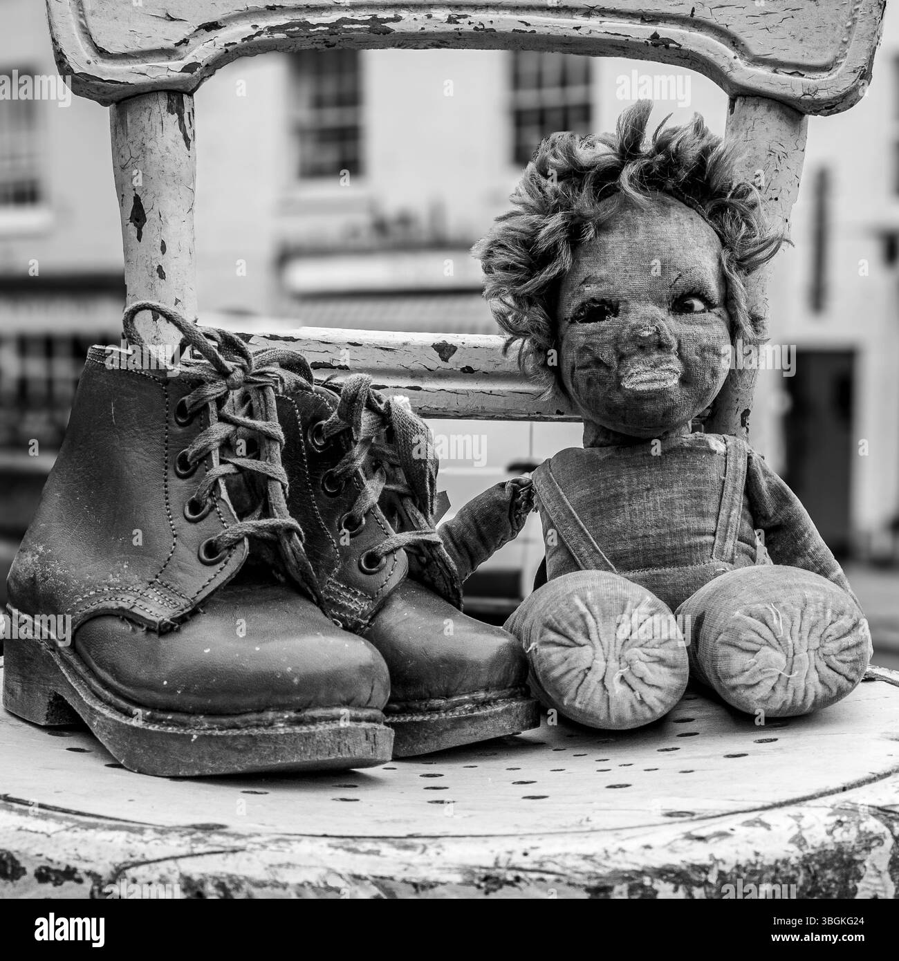 Mostra d'epoca inquietante: Una bambola intemprata e stivali indossati su una sedia sbiadita a Bridport Street Market, Dorset. Immagine in bianco e nero. Foto Stock