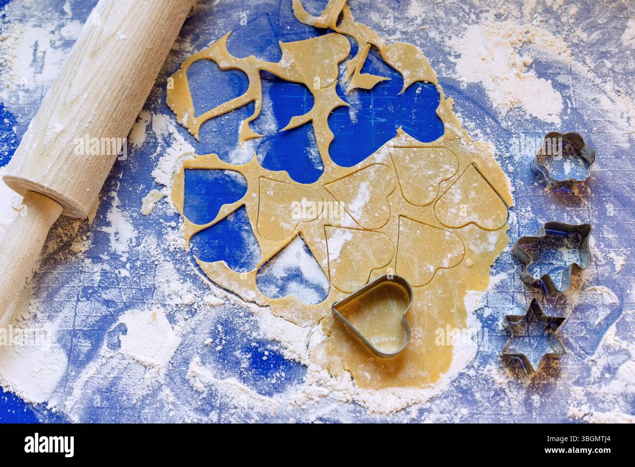 impasto arrotolato per biscotti al burro con taglierine per biscotti e rullo per torte su una base in silicone blu Foto Stock