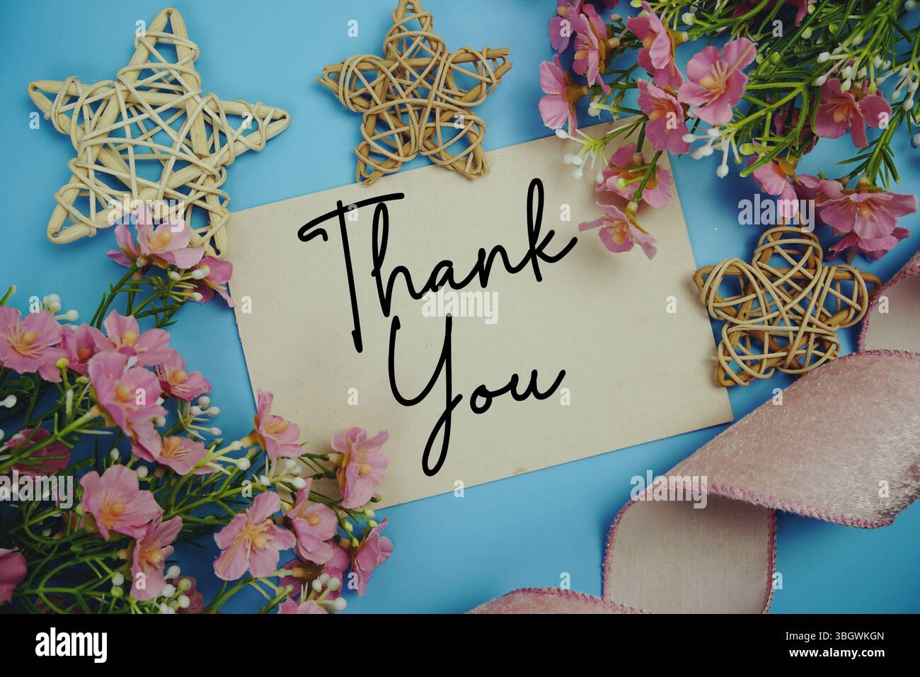 Testo di ringraziamento su carta con nastro in tessuto e decorazioni a stelle in rattan su sfondo blu Foto Stock