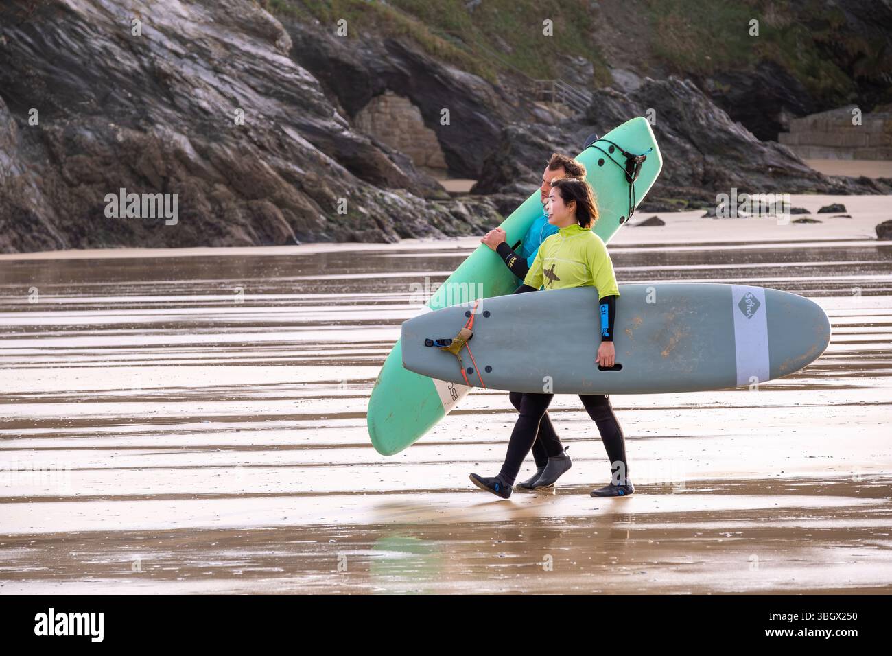Un istruttore di surf e uno studente che trasporta le tavole da surf e cammina fino al mare a Towan Beach a Newquay in Cornovaglia, Regno Unito. Foto Stock