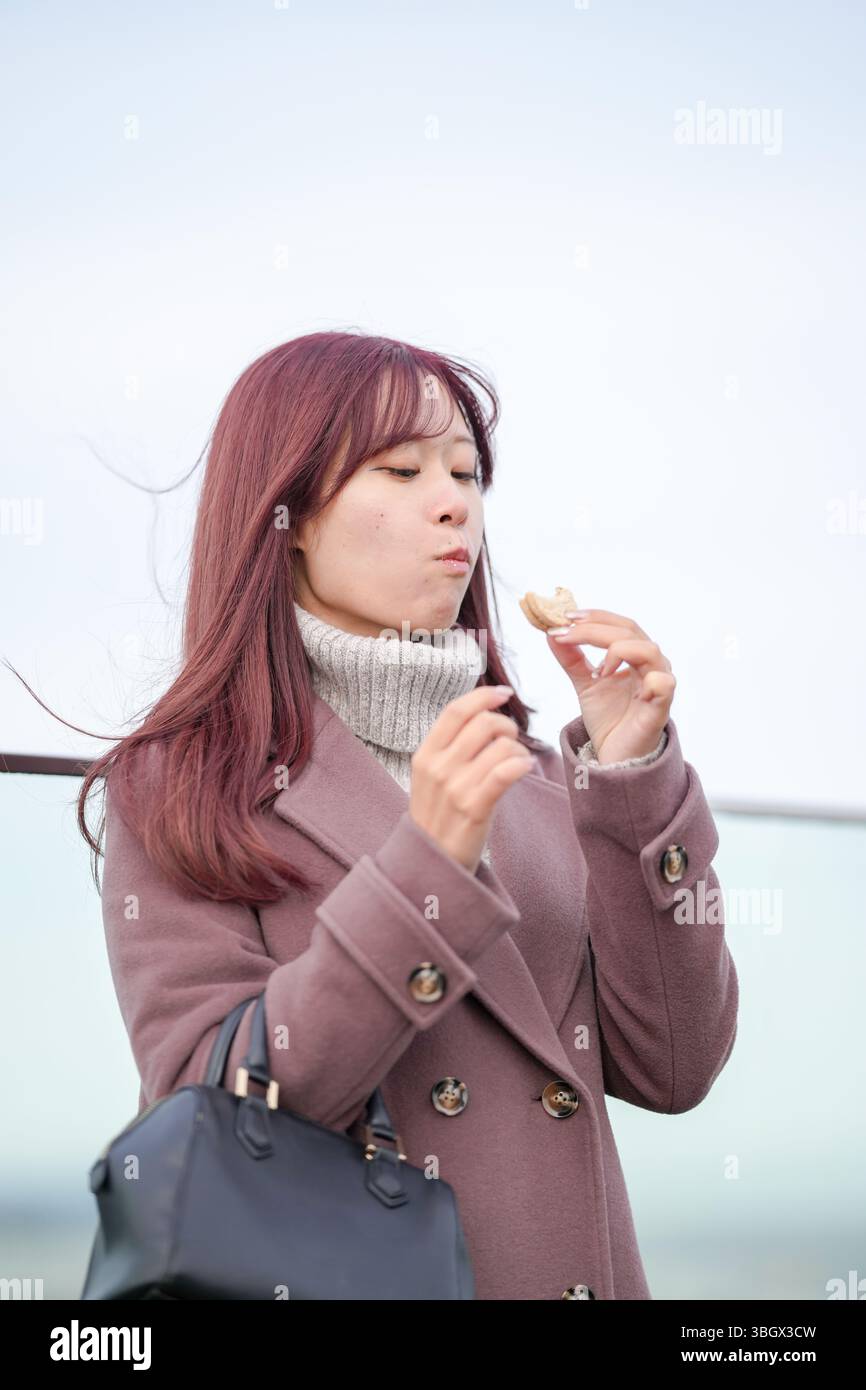 In una fredda mattina di dicembre, una donna giapponese di vent'anni con lunghi capelli rosa e un trench rosa si erge su un tetto sopra la città. Sorridere, Foto Stock
