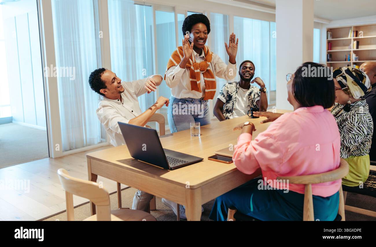 Un team allegro e variegato di colleghi che celebrano un successo attorno a un tavolo in un ufficio contemporaneo. L'atmosfera sottolinea l'importanza del coll Foto Stock