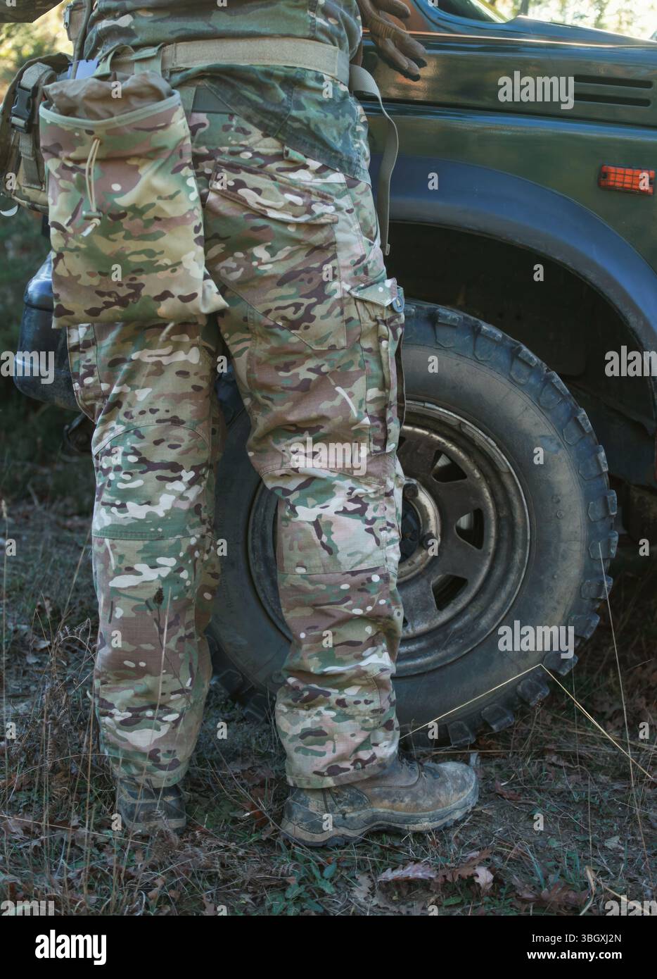 Soldato rivestito di pantaloni mimetici e stivali tattici si trova vicino al volante di un veicolo militare, impegnato in esercizi di allenamento che enfatizzano la prontezza al combattimento e il lavoro di squadra Foto Stock