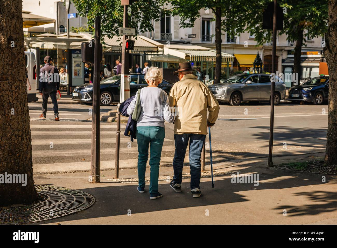 Una vista mozzafiato da dietro di una coppia anziana che cammina insieme lungo un marciapiede soleggiato della città, l'uomo che usa un bastone, incarna una vita di compa Foto Stock