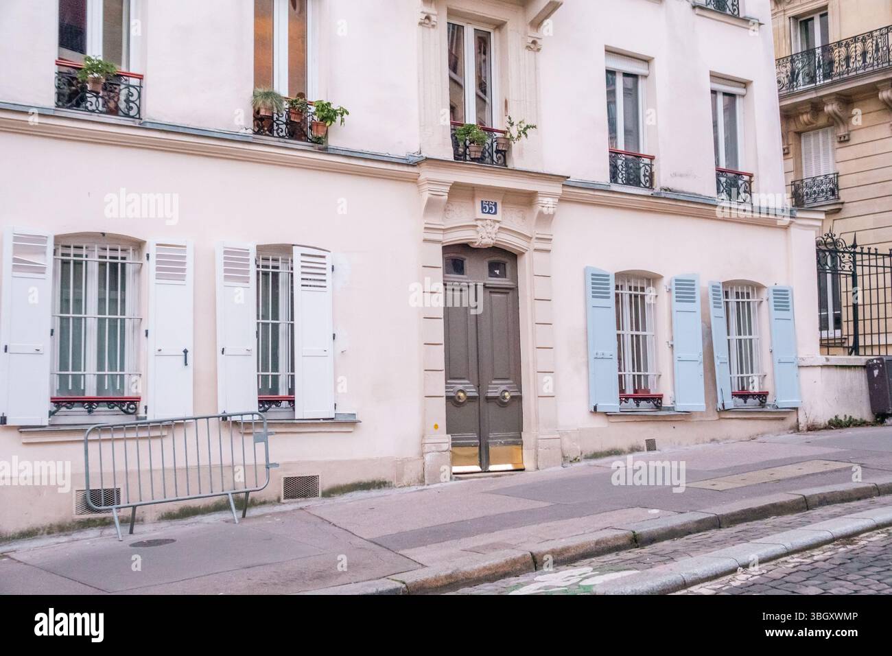 La facciata di un affascinante edificio residenziale parigino presenta una doppia porta grigia, finestre con persiane azzurre e fioriere. L'edificio Foto Stock