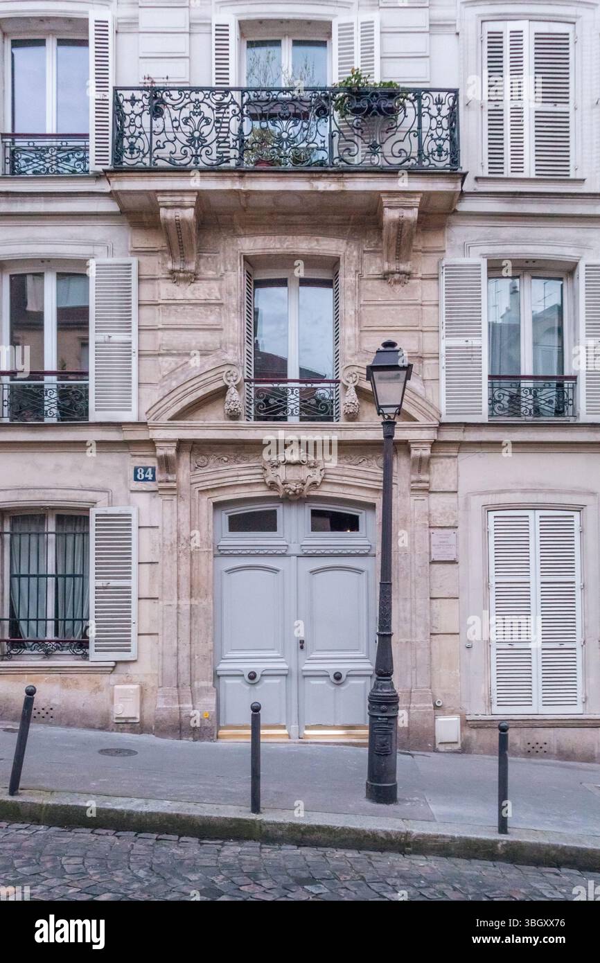 L'elegante entrata di un edificio parigino (numero 84) presenta una doppia porta grigia pallida, un balcone ornato in ferro battuto sopra e una classica l nera Foto Stock
