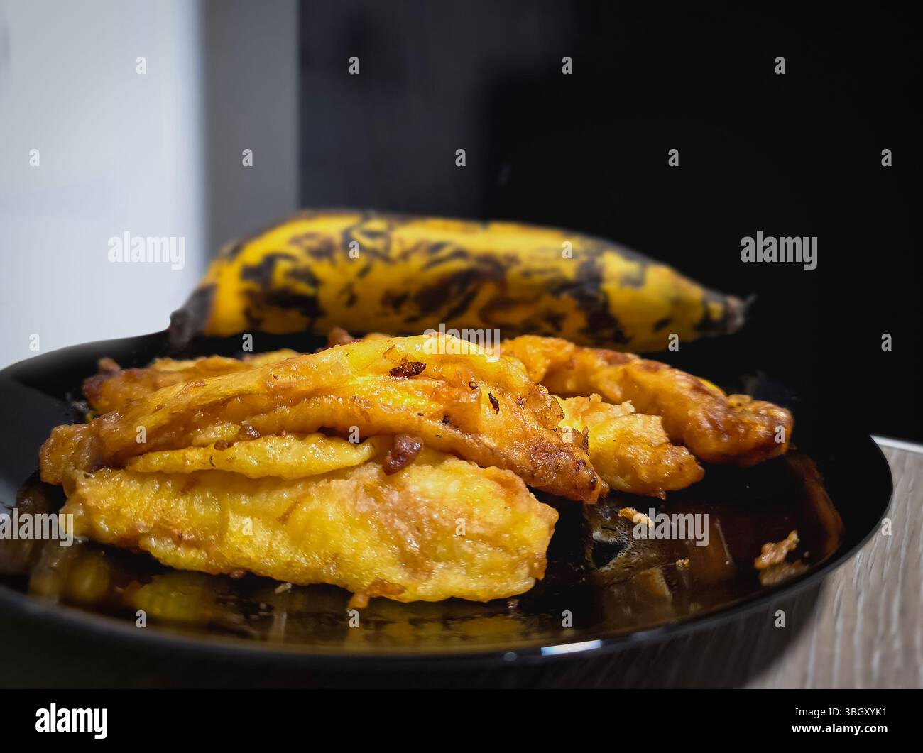 Immagine ravvicinata di autentici frittelle di banana pori del Kerala con banana planante su piatto nero Foto Stock