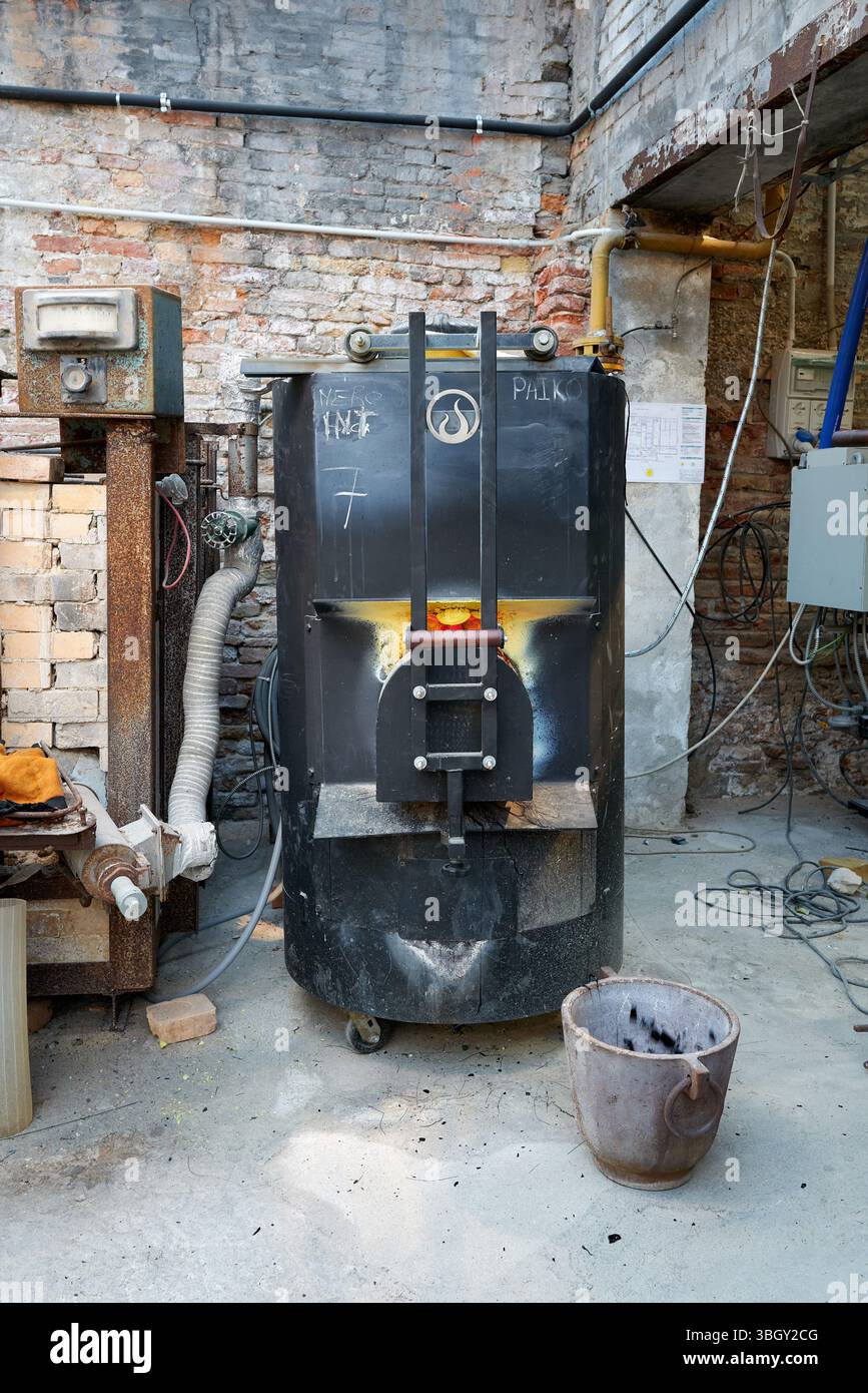 Interno della vetreria di Murano che mostra un forno utilizzato nel processo di fusione del vetro. Circondato da attrezzature industriali e muratura storica Foto Stock