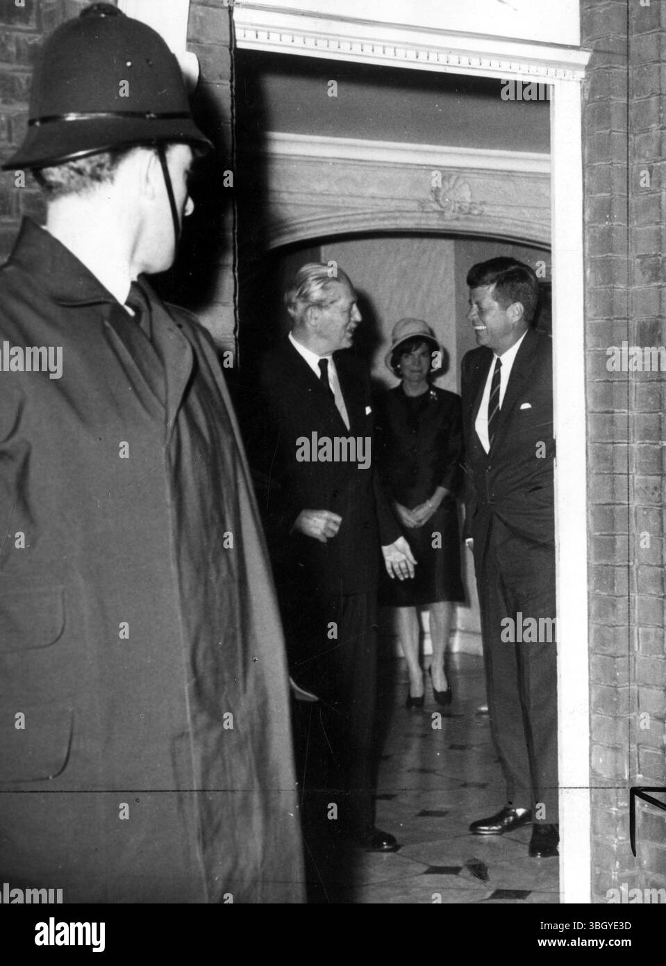 Un poliziotto londinese fa capolino mentre il presidente John Fitzgerald Kennedy (a destra) parla con il primo ministro britannico Harold Macmillan nel corridoio della casa di Buckingham Place del principe e della principessa Radziwill. Nella foto c'è anche la moglie del presidente Jacqueline. 4 giugno 1961 Foto Stock