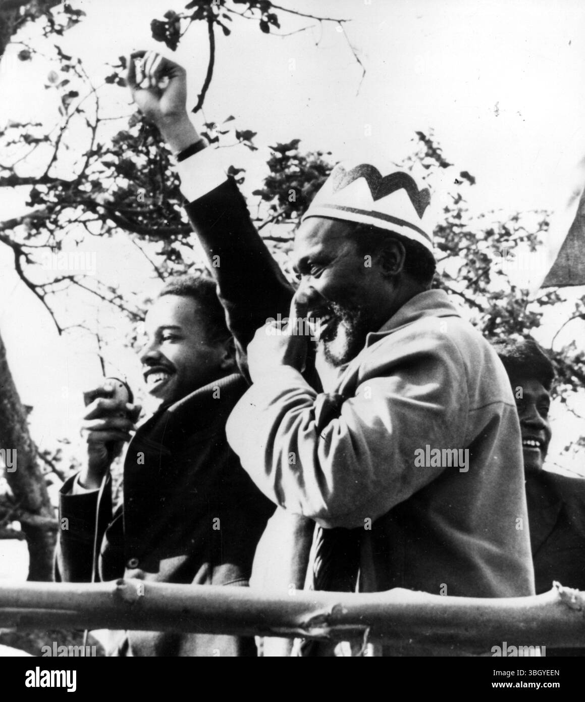 Il diciannovenne Peter Kennet (a sinistra) alza il braccio, l'indice esteso nel saluto di Kanu Unity mentre si rivolge a una folla di circa 66.000. Accanto a lui (a destra) guardando ogni centimetro il padre orgoglioso è il leader Kanu Jomo Kenyatta. Jomo Kenyatta si stava rivolgendo alla folla quando improvvisamente chiese se volevano vedere suo figlio. Con un ruggito di approvazione, il giovane attacco keniota si è messo sulla piattaforma oltre a suo padre. 25 luglio 1962 Foto Stock