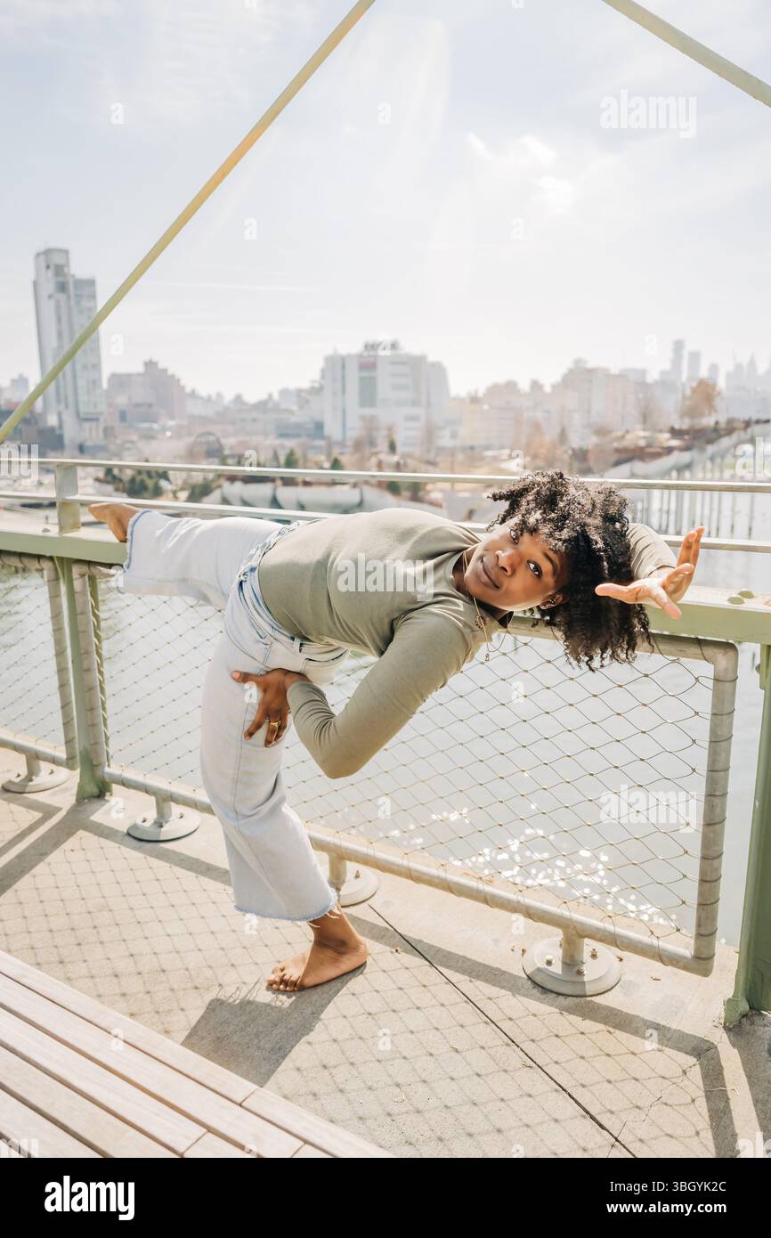 Il ballerino si bilancia su una gamba sopra la ringhiera con lo skyline della città alle spalle Foto Stock