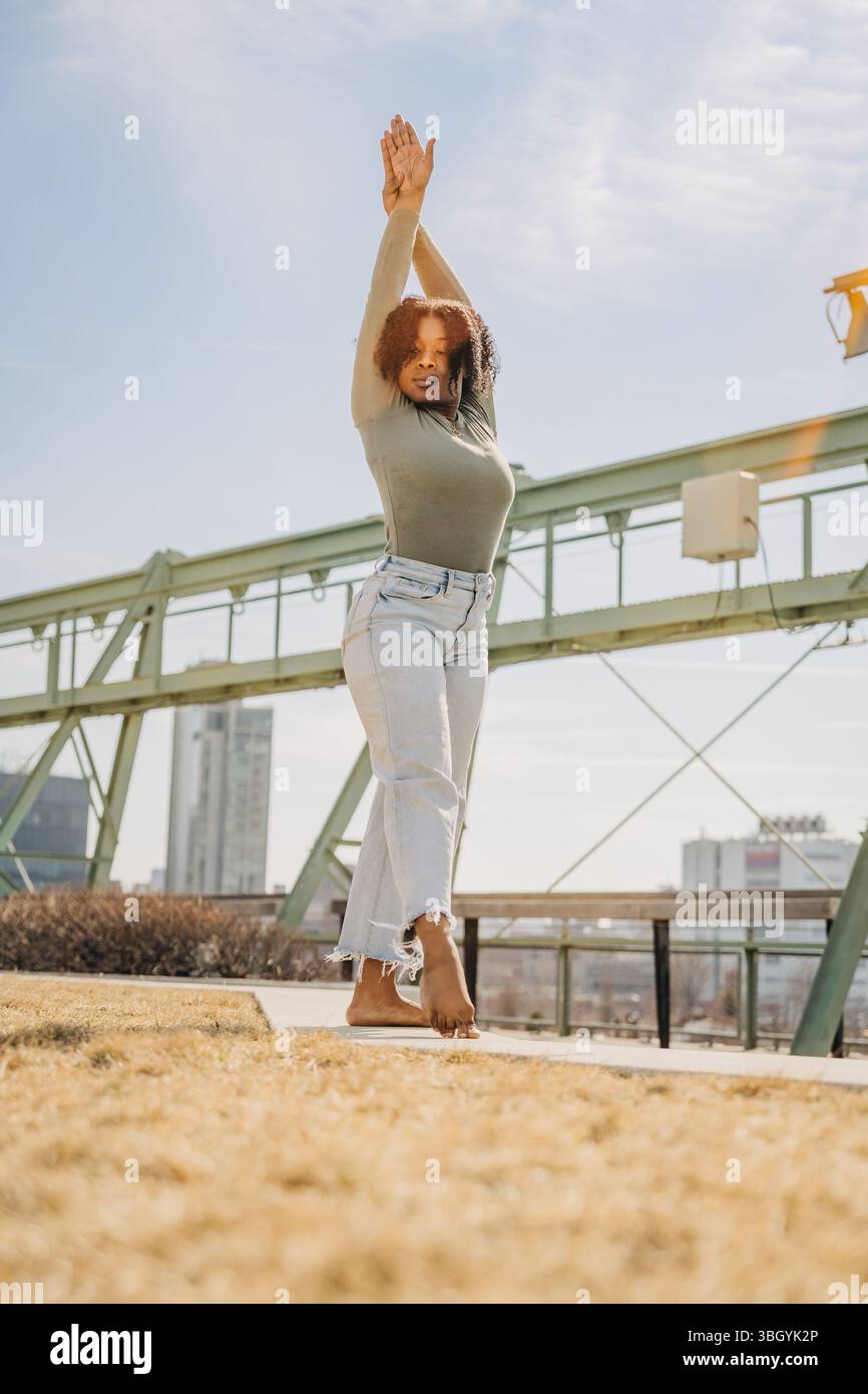 La ballerina sta a piedi nudi nell'erba con le braccia sollevate sotto il cielo luminoso Foto Stock