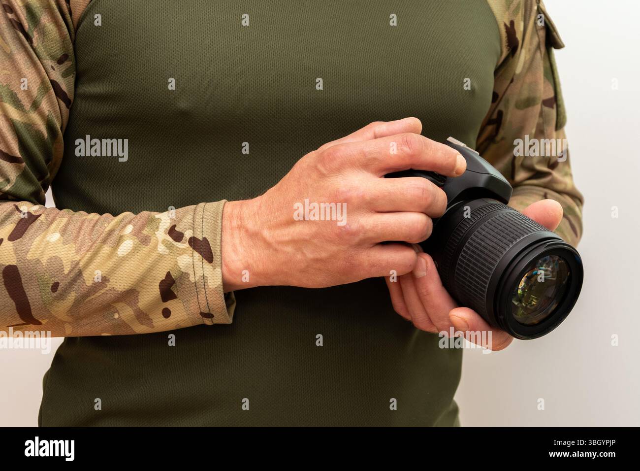 Professionista in costume militare con fotocamera reflex. Sfondo bianco, concetto di ripresa militare e reportage fotografico Foto Stock