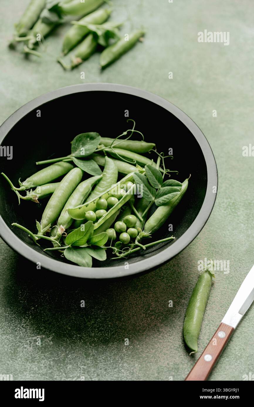 Piselli verdi freschi in cialde e fagioli in un recipiente nero Foto Stock