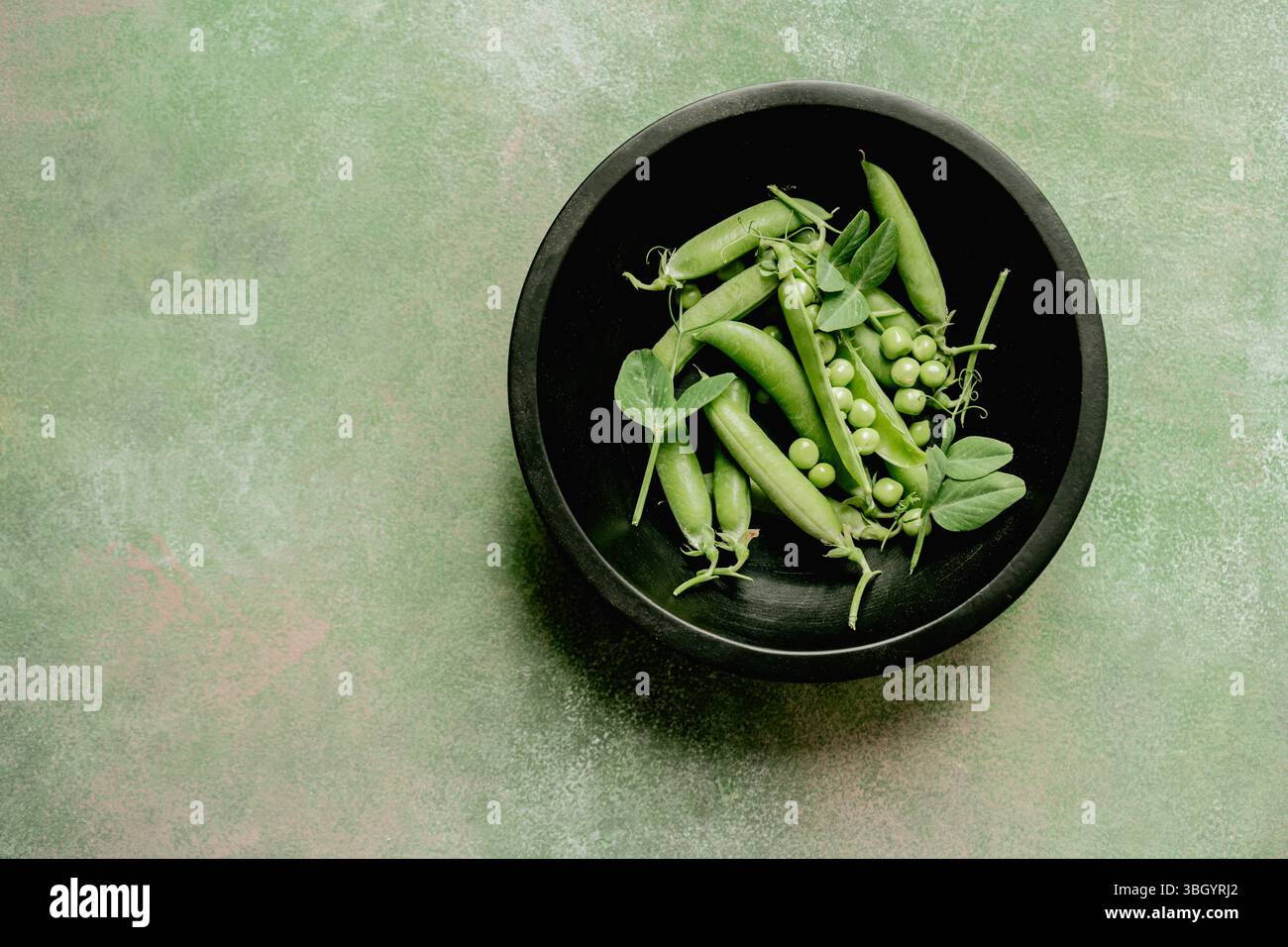 Piselli verdi freschi in cialde e fagioli in una ciotola nera, copia spazio Foto Stock