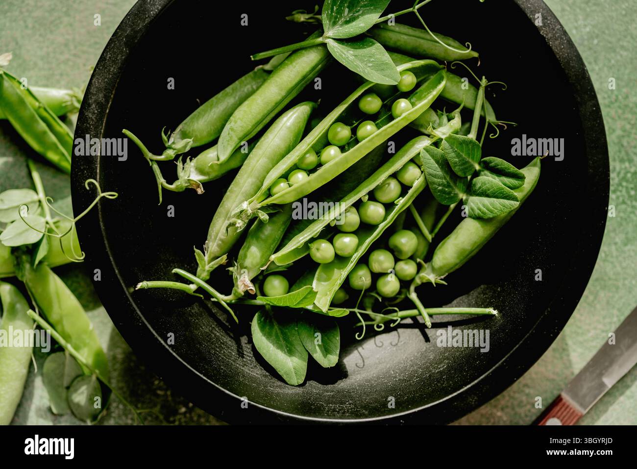 Piselli verdi freschi in cialde e fagioli in un recipiente nero Foto Stock