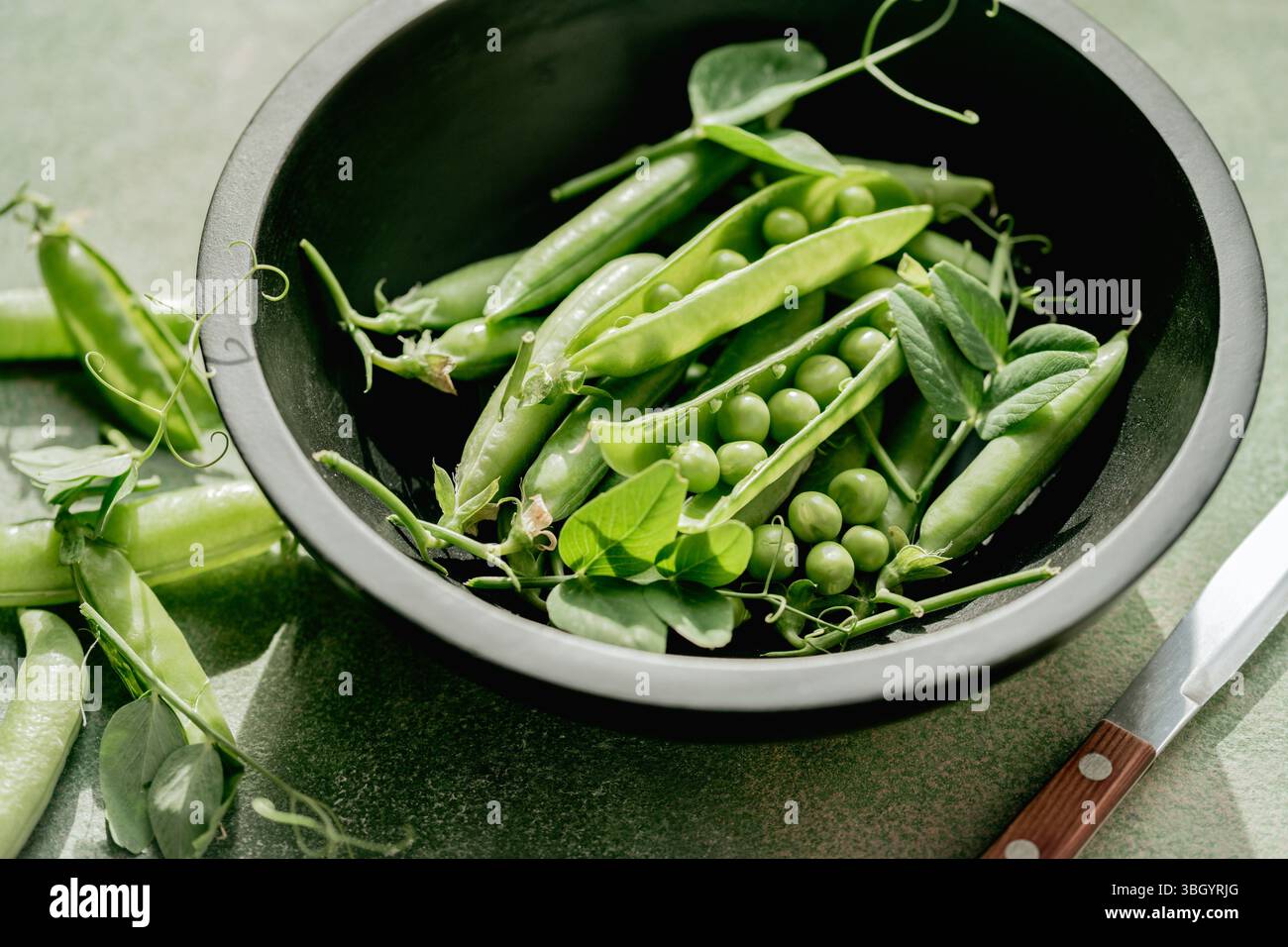 Piselli verdi freschi in cialde e fagioli in un recipiente nero Foto Stock