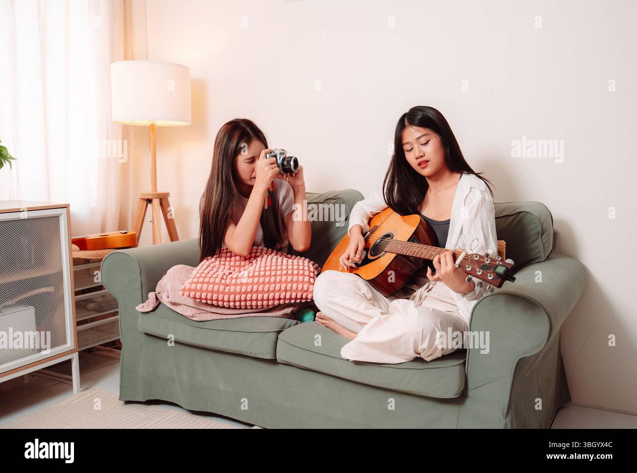 Donna asiatica musica chitarra che suona insieme canzone Teenage soggiorno interno, gioiosa riunione di amici condividere musica, Risate e relax Foto Stock