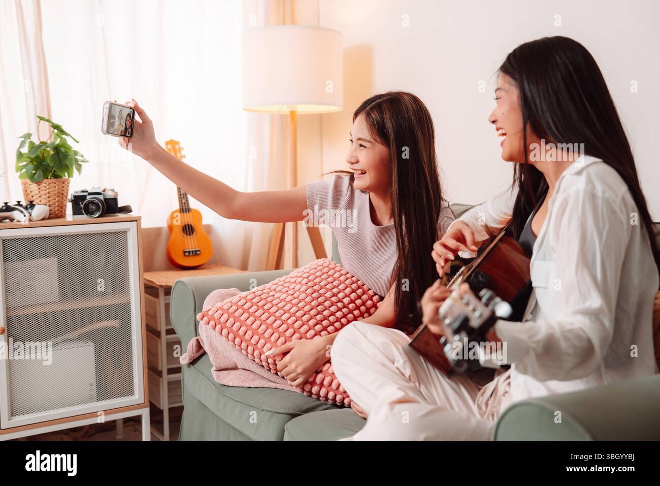 Donna asiatica musica chitarra che suona insieme canzone Teenage soggiorno interno, gioiosa riunione di amici condividere musica, Risate e relax Foto Stock