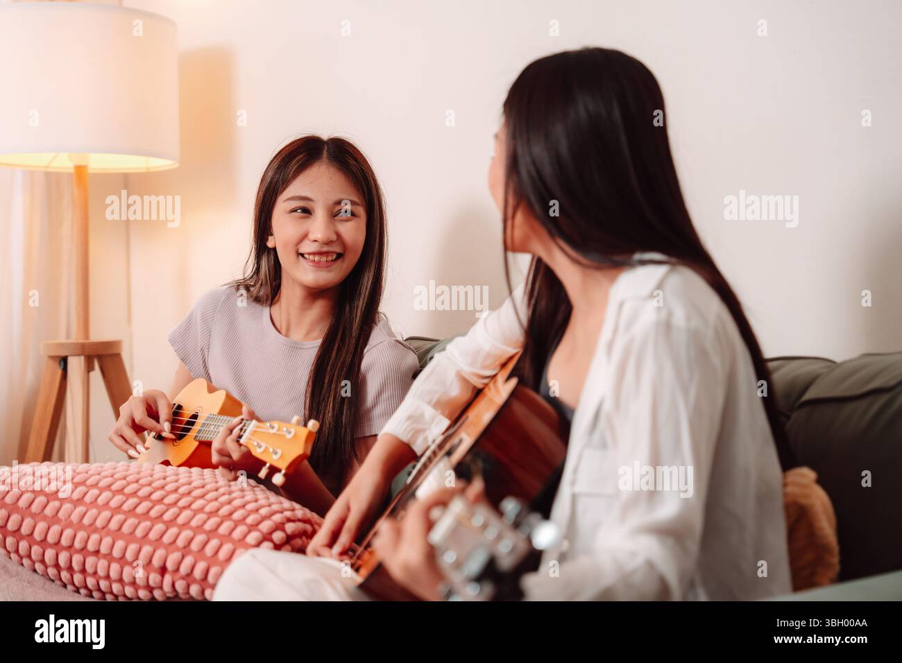 Donna asiatica musica chitarra che suona insieme canzone Teenage soggiorno interno, gioiosa riunione di amici condividere musica, Risate e relax Foto Stock