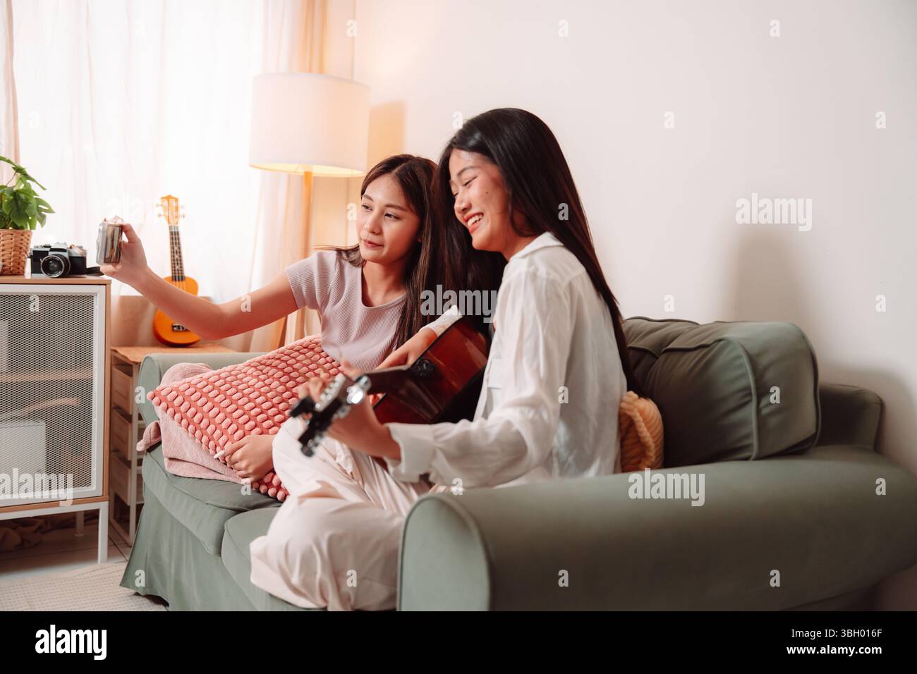 Donna asiatica musica chitarra che suona insieme canzone Teenage soggiorno interno, gioiosa riunione di amici condividere musica, Risate e relax Foto Stock