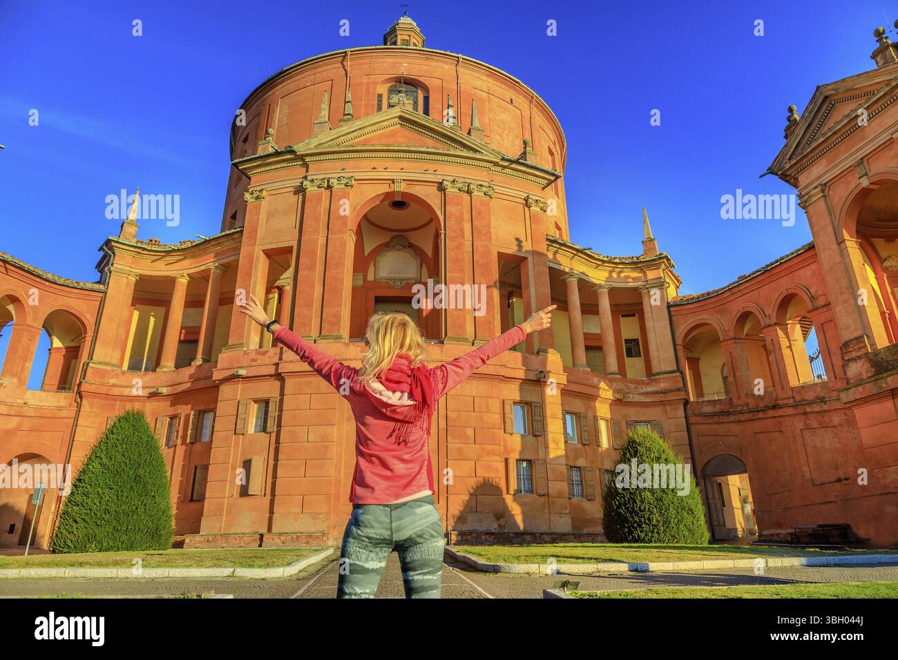 Donna spensierata a braccia aperte al Santuario della Madonna di San Luca. Popolare destinazione turistica a Bologna, Italia. Donna bionda che gode dell'istore Foto Stock