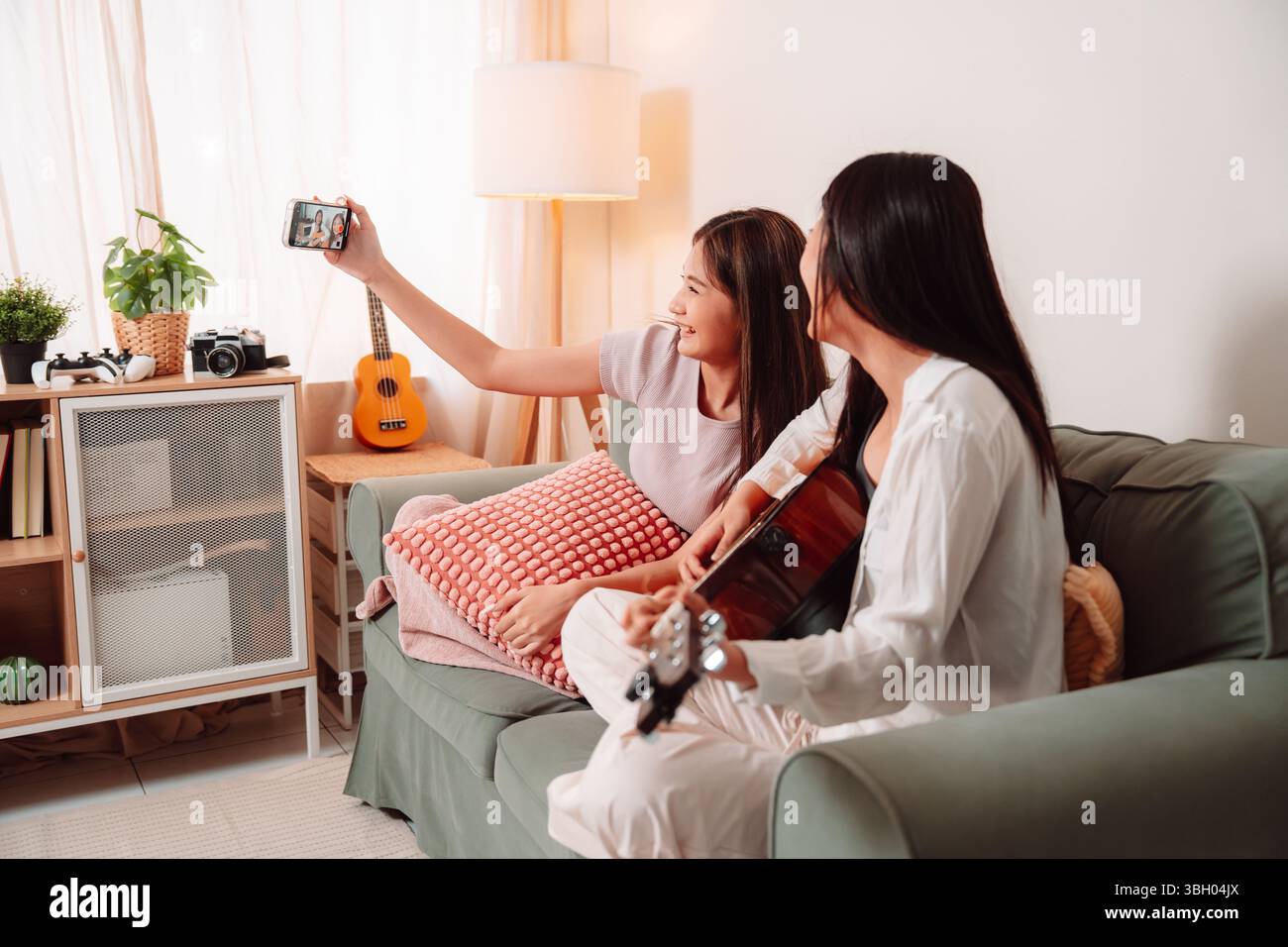 Donna asiatica musica chitarra che suona insieme canzone Teenage soggiorno interno, gioiosa riunione di amici condividere musica, Risate e relax Foto Stock