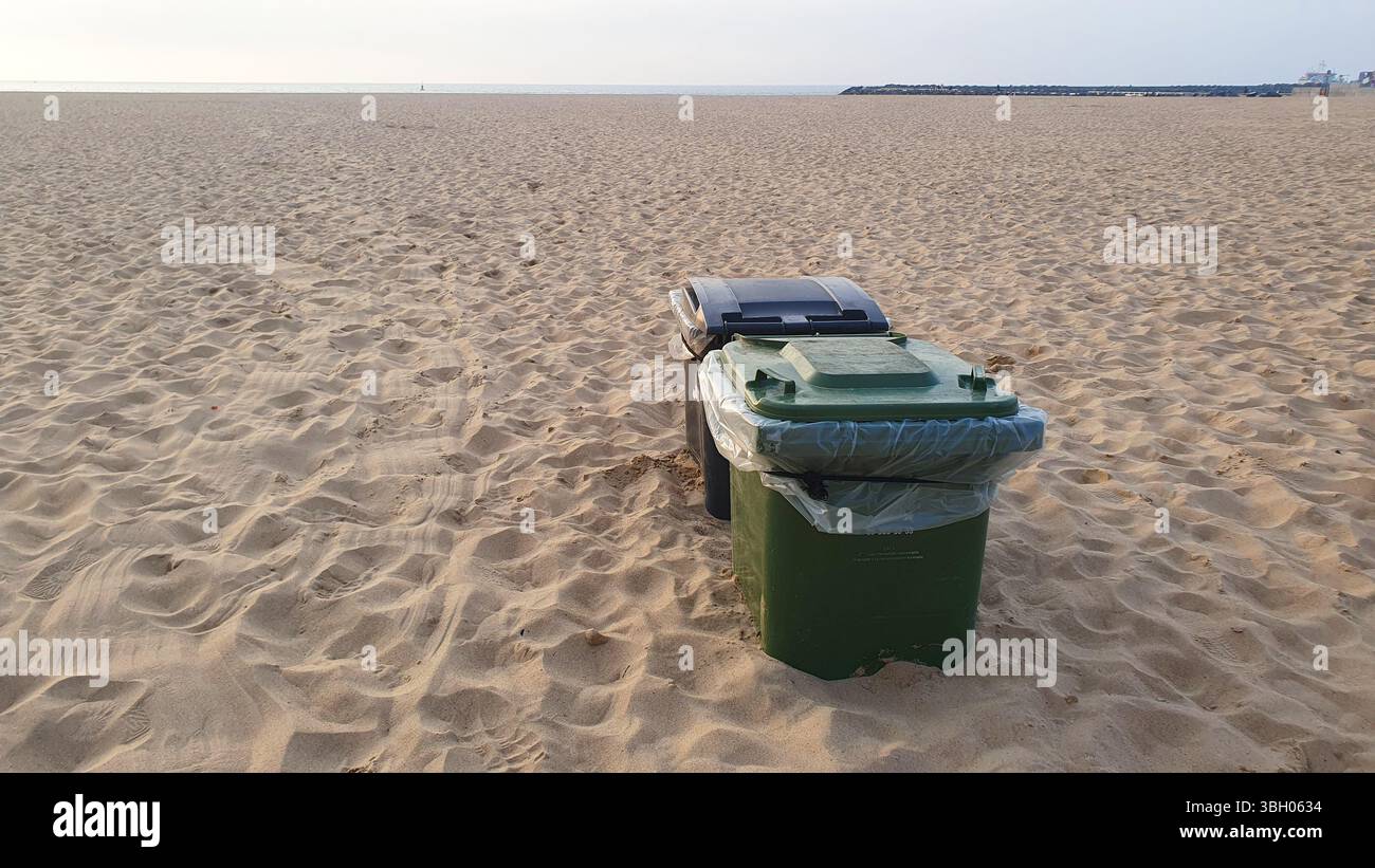 Contenitori per rifiuti di plastica neri e verdi sepolti in sabbia gialla sulla spiaggia. Foto Stock