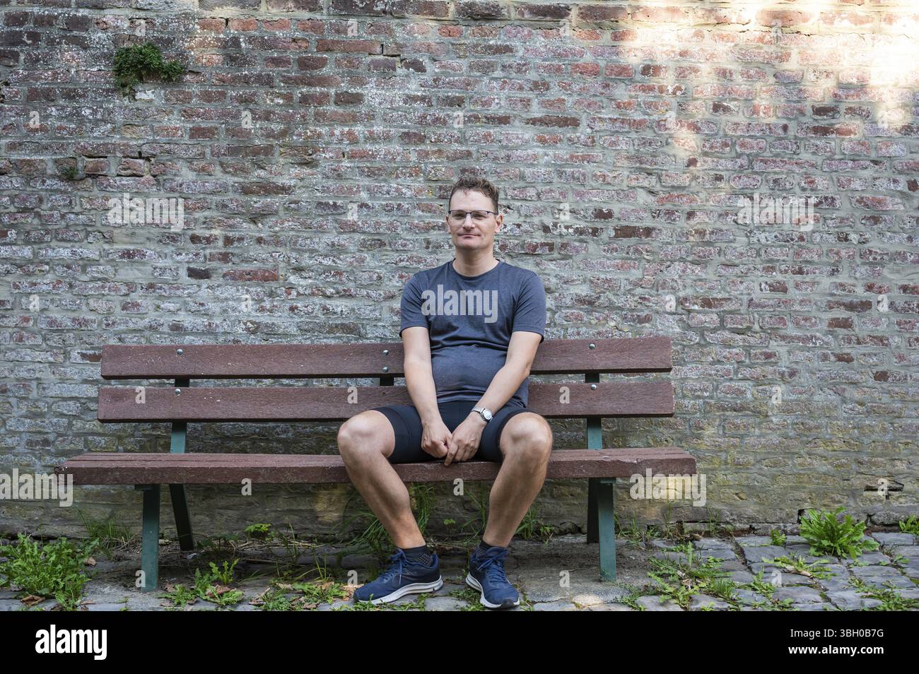 Sportivo ragazzo di 45 anni seduto su una panchina con un muro di mattoni sullo sfondo, Grez, Brabant Wallon, Belgio. Modello rilasciato Foto Stock
