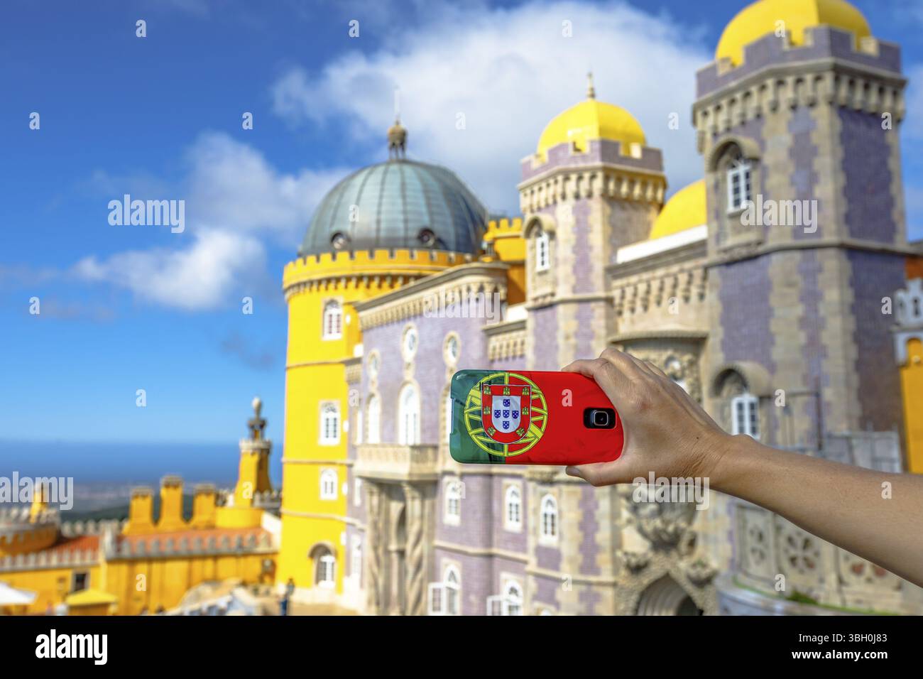 La donna scatta una foto del Palazzo Nazionale da pena con il cellulare con la copertura della bandiera del Portogallo. Turismo e viaggi in Portogallo. Il castello di pena è patrimonio dell'UNESCO Foto Stock